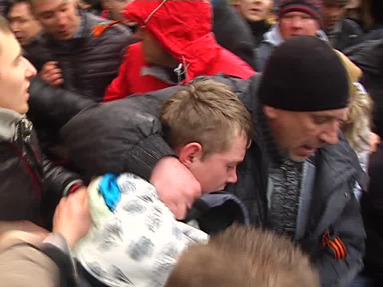 Скриншот видео. Человек с георгиевской лентой пытается защитить молодого человека от ударов толпы